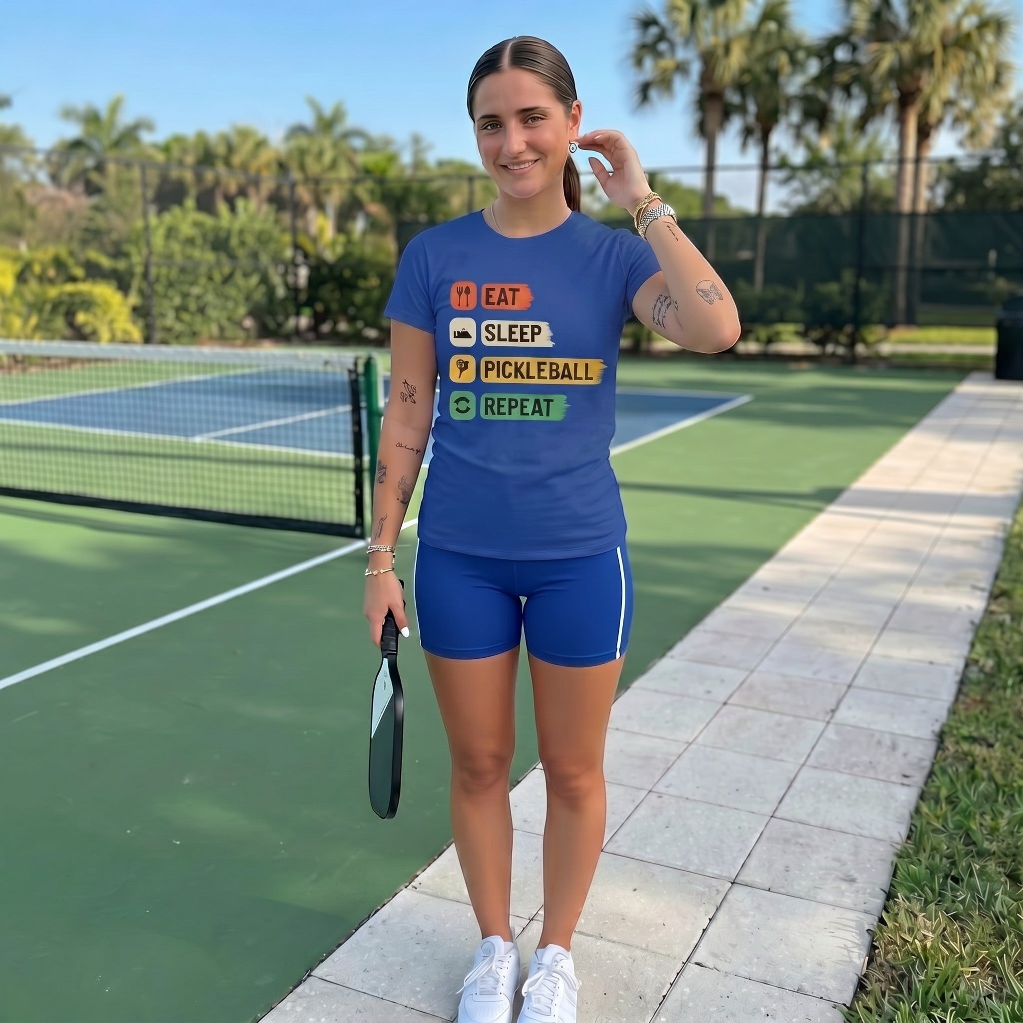 TrendyShift.Com blue cotton pickleball t-shirt with Eat Sleep Pickleball Repeat graphic worn by a woman on a court.